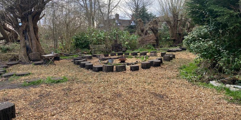 Outdoor circle of tree stump seats around a fire pit in a woodland area.