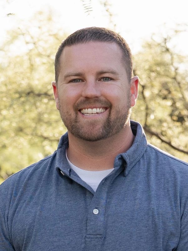 Smiling man in a blue shirt outdoors with a natural background.