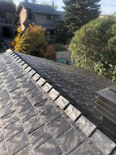 Sunlit slate roof on a residential building with trees in the background.
