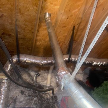 Ductwork and pipes in an attic space with wooden beams.