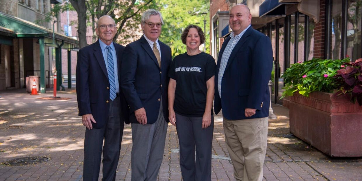 Four people posing in a sunny outdoor alley.