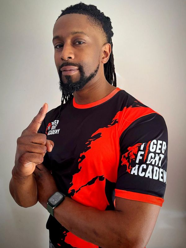 Man in a black and red Tiger Fight Academy shirt showing a thumbs-up gesture.