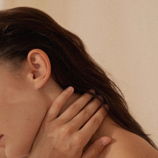 Close-up of a woman touching her neck with her hand.