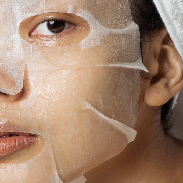 Close-up of a person wearing a moisturizing facial sheet mask with a white towel wrapped around their head.