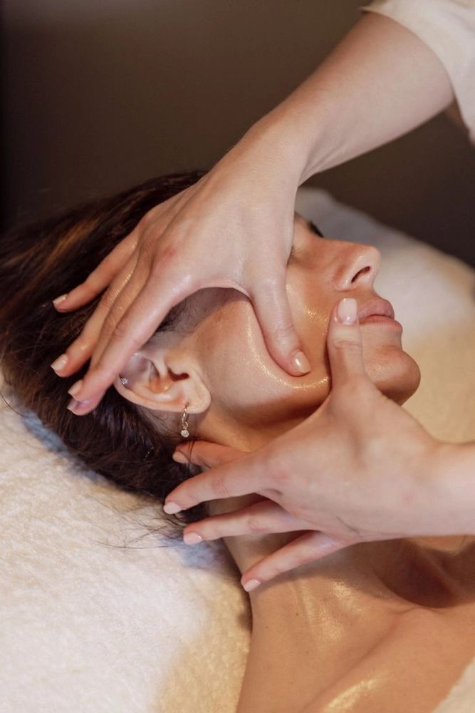 Spa essentials including towels, green bath salts, oil, and flowers on a wooden surface.