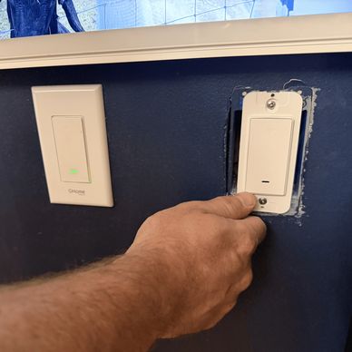 Hand adjusting a light switch on a dark blue wall.