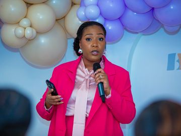 Woman in a pink suit speaking with a microphone at an event.