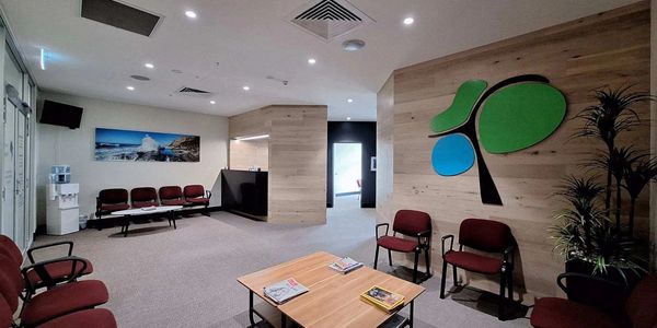 Modern waiting room with maroon chairs, wooden tables, and a colorful wall design.