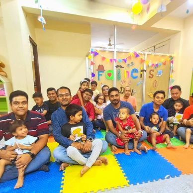 A group of adults and children gathered for a colorful birthday celebration indoors.
