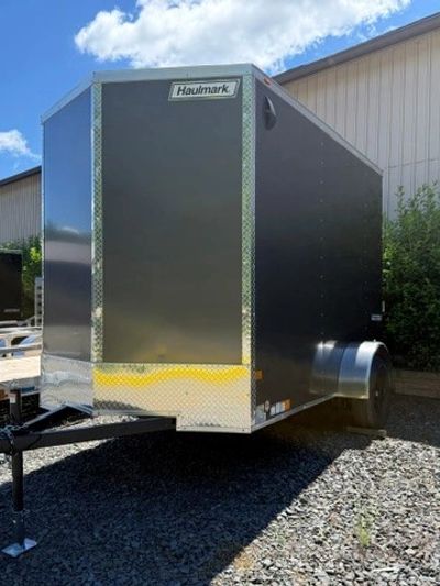 Black Haulmark enclosed cargo trailer parked on gravel under a blue sky.