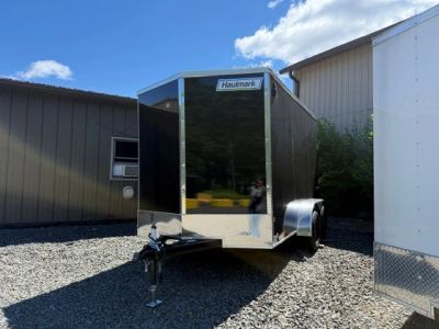 Black Haulmark enclosed trailer parked on gravel under blue sky.