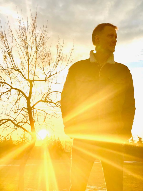 Pierre Sabourin debout avec un couché de soleil et des arbres en arrière plan