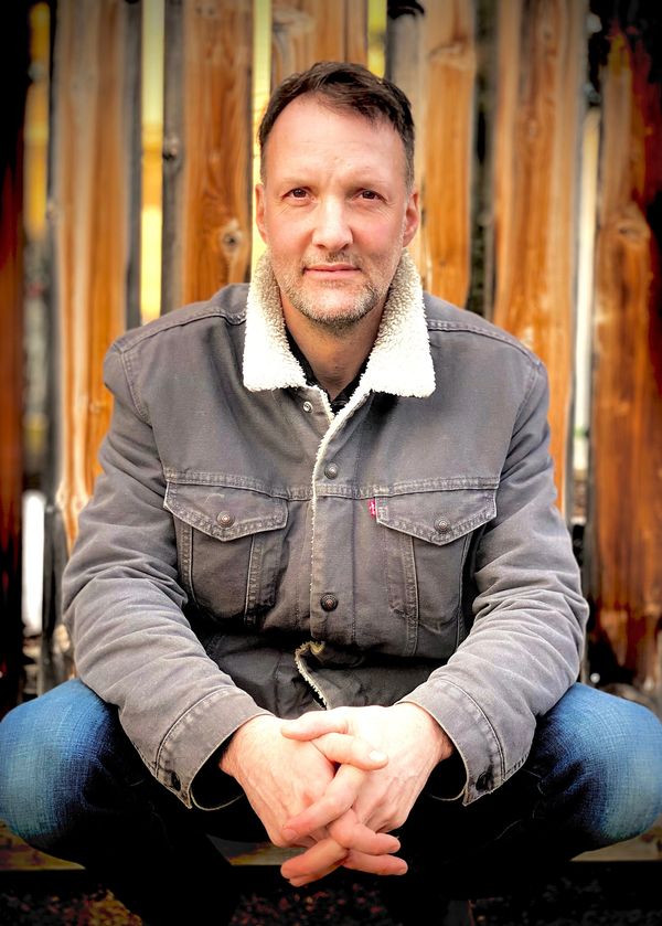 Pierre Sabourin assis avec du bois en arrière plan