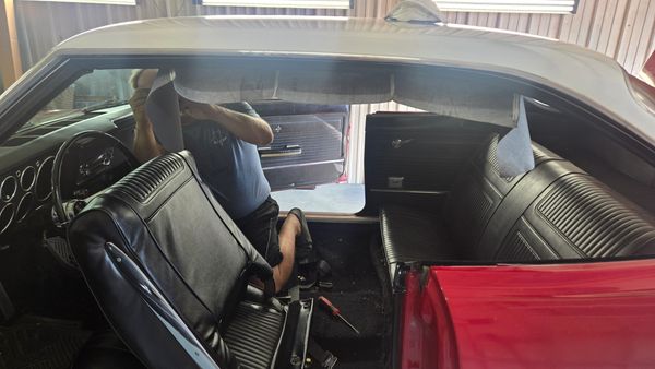 Man working on car interior upholstery inside a vintage red vehicle.