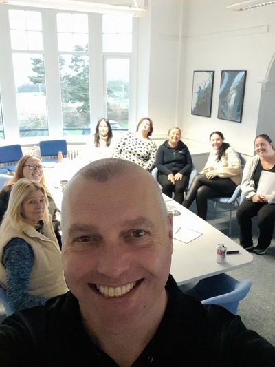 Professional trainer, Wil, with a group of women sitting in a room for workplace-based training.