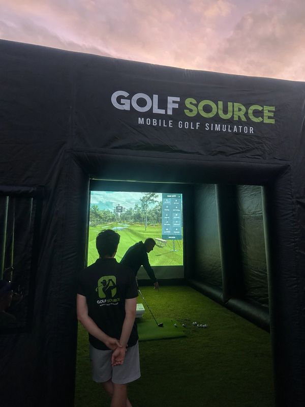 People playing golf in a mobile golf simulator tent at sunset.
