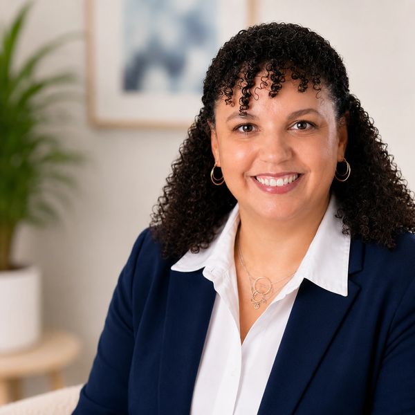 Smiling woman with curly hair in a navy blazer and white shirt.