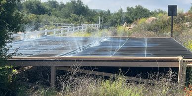 Solar panels being irrigated with water sprays in a natural outdoor setting.