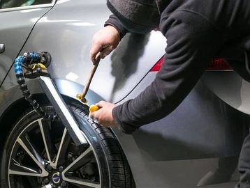 Person repairing car dent with specialized tools.