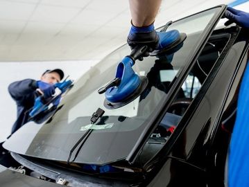 Technicians installing a windshield using suction cups.