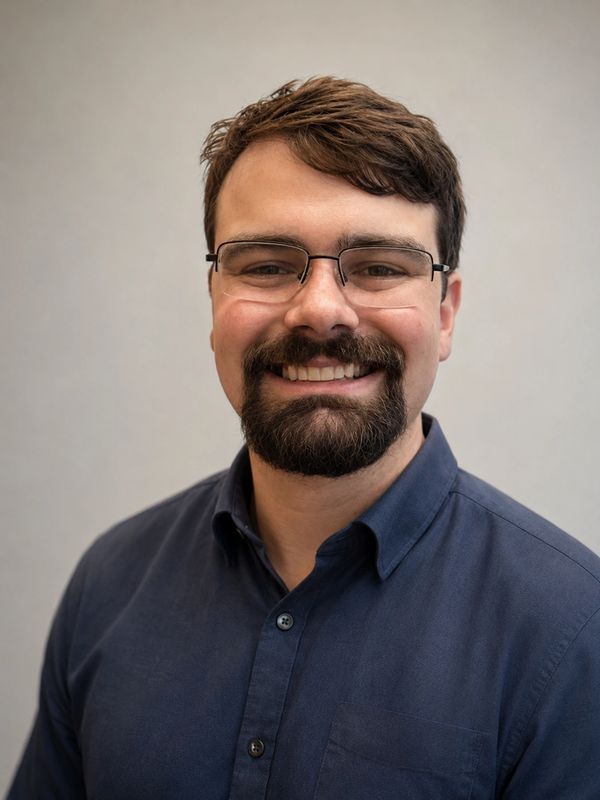 Man with glasses and beard smiling in a navy shirt.