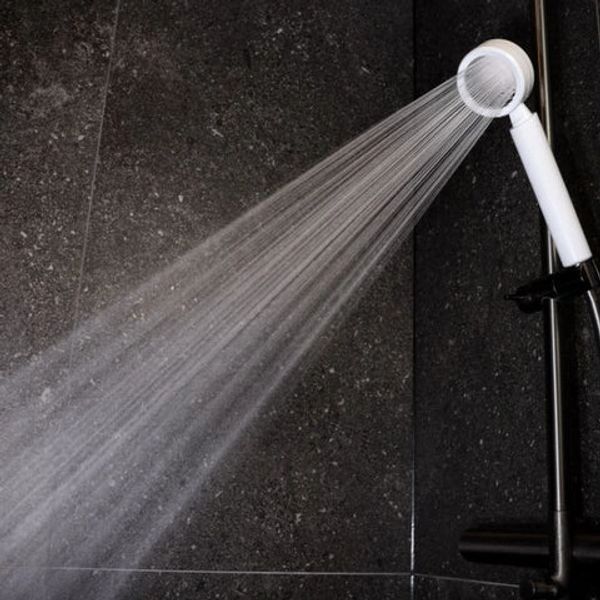 White handheld shower head spraying water against dark tiled wall.