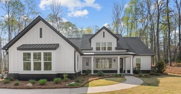 Modern white farmhouse with black roof and large windows in a wooded area.