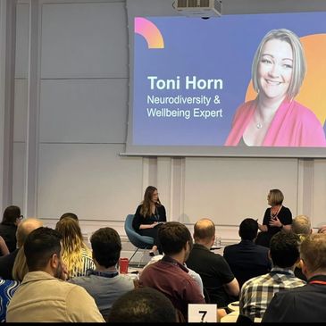 Toni Horn, Neurodiversity & Wellbeing Expert, speaking at a live event with audience engagement.