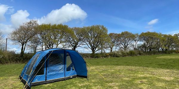 Blue tent pitched on grassy field under a partly cloudy sky.
