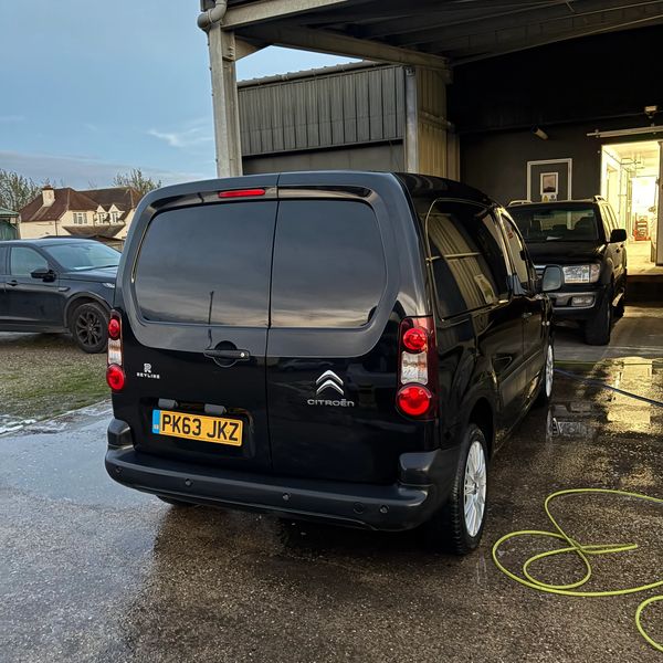 Black Citroën van parked outside a garage on a wet concrete surface.