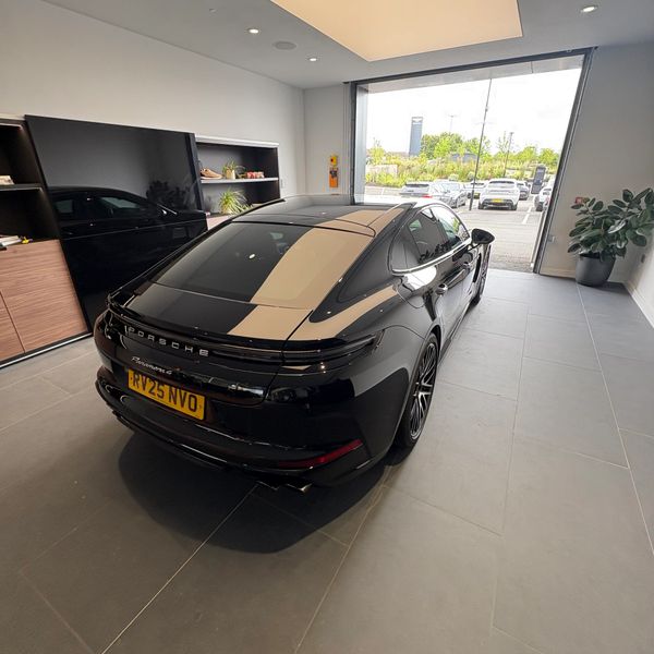 Black Porsche Panamera parked inside a modern showroom with open doors.