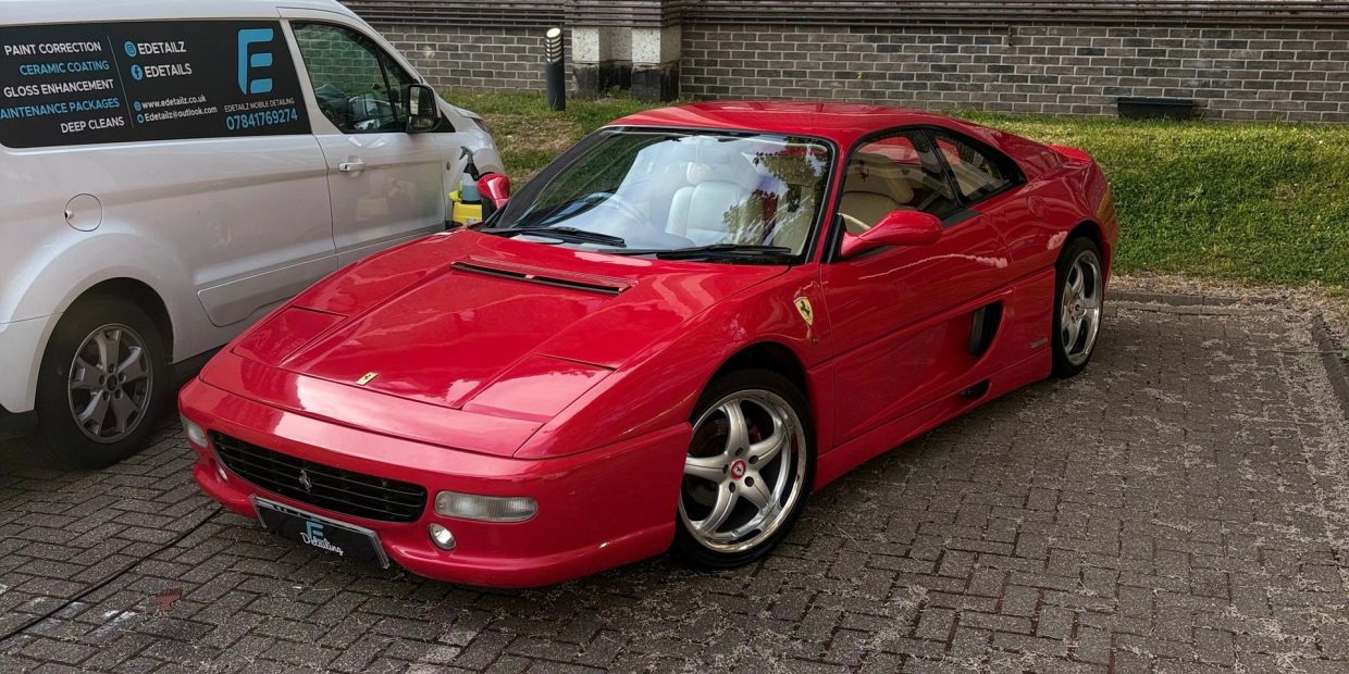 Shiny red Ferrari sports car parked beside a white van.