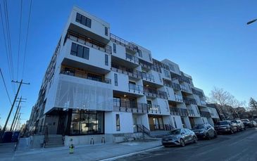 Modern multi-story apartment building with balconies and parked cars.