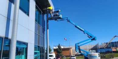 Worker on a blue boom lift cleaning building windows.