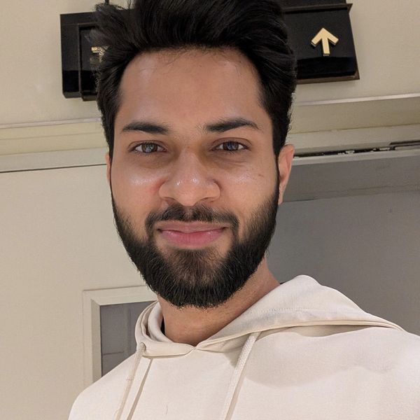 Young man with a beard wearing a cream hoodie, smiling indoors.