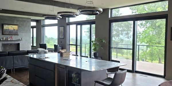 Modern kitchen with marble island and large windows overlooking greenery.