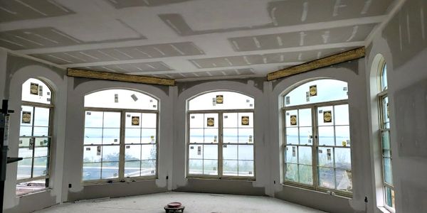 Spacious room under construction with large arched windows and drywall installation.
