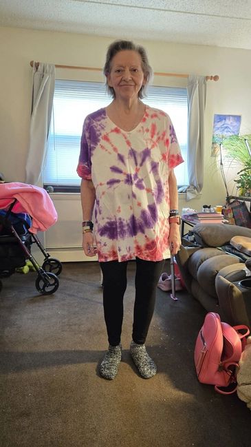 Smiling elderly woman in tie-dye shirt and black leggings.