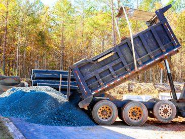 Dump truck unloading gravel at a construction site surrounded by trees during daytime