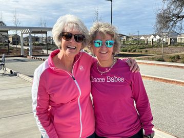 Two women smiling outdoors, dressed in pink sportswear.