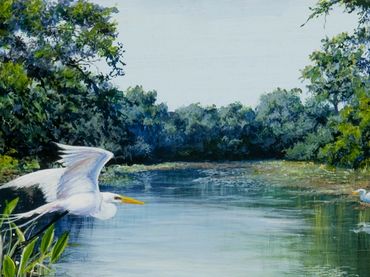 White egret flying over a pond with other egrets on the shore