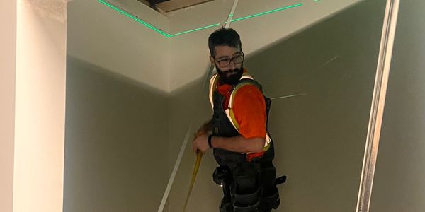 Worker on stilts measuring a corner wall with a tape measure.