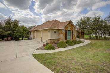 A single-story house with stone accents and a large driveway under a cloudy sky.