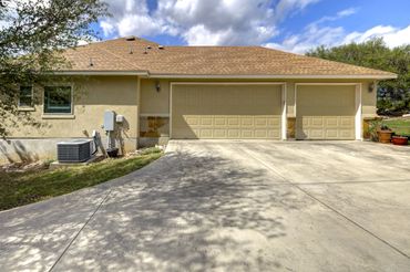 Suburban house with a three-car garage and concrete driveway under a partly cloudy sky.