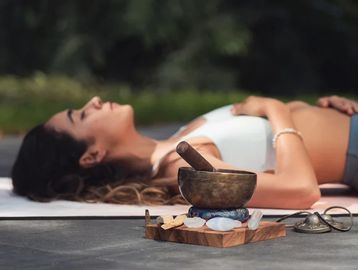 Woman lying down with hand on heart and stomach next to a sound bowl with crystals