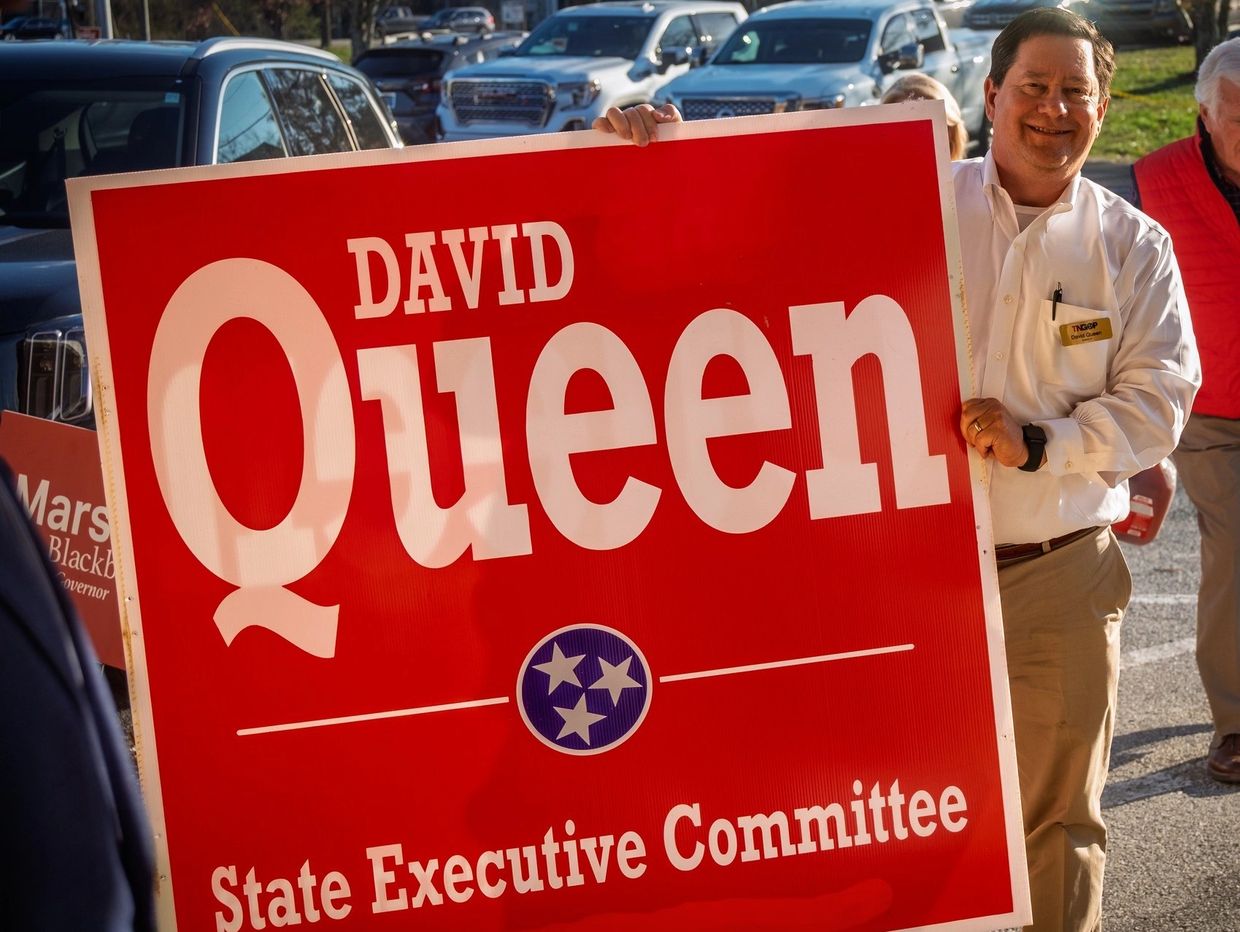 A man holding a large red State Executive Committee campaign sign for David Queen.
