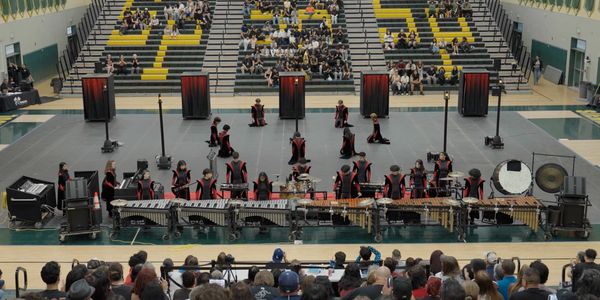 Indoor percussion ensemble performing in a gymnasium with an audience watching.