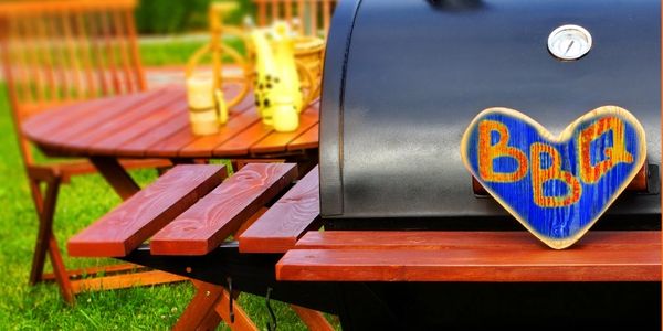 Heart-shaped BBQ sign on a charcoal grill in a backyard setting.
