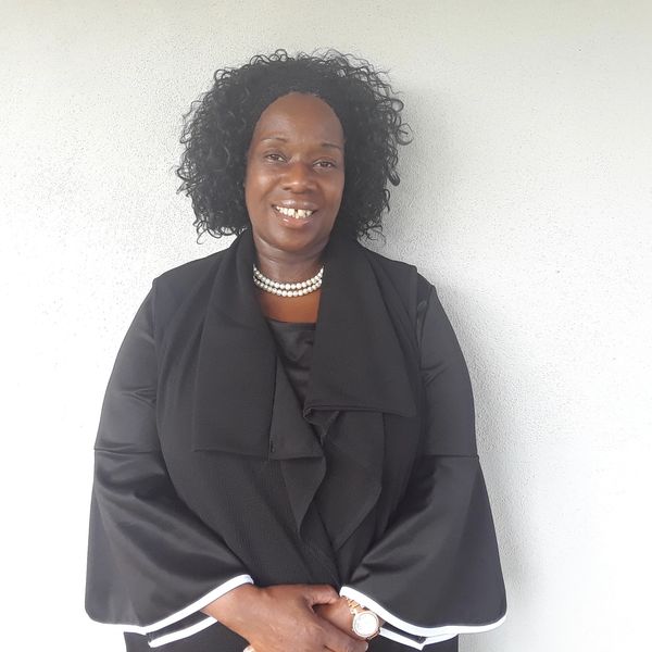 Woman smiling in black outfit with pearl necklace.