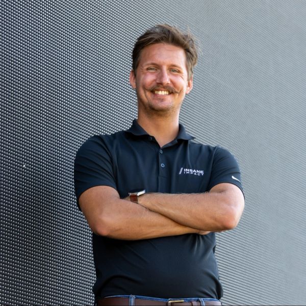 Confident man with a mustache wearing a black polo shirt, standing with arms crossed.